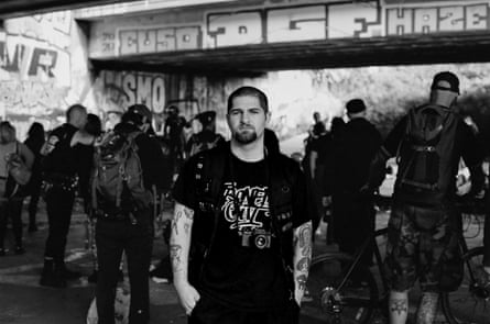 Black and white photo of Jamie Golberg standing among a crowd of punks in front of a graffitied wall