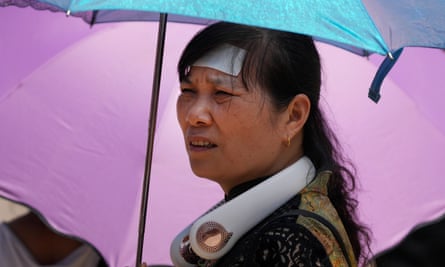 A woman wearing an electric fan, putting a cooling pad on her forehead and carrying an umbrella visits the Forbidden City on a sweltering July day in Beijing