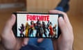 A person holding a phone screen which has the word 'Fortnite' displayed on it