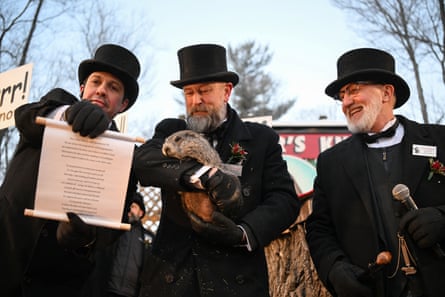 Three men in black coats and top hats, one of the holding a groundhog and another a scroll