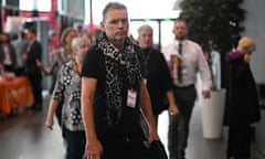 Dale Vince walking in the entry area of a conference hall, wearing a lanyard and a scarf