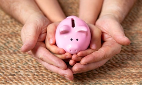 A pair of male adult hands cradles a pair of child's hands cradling a pink piggy bank