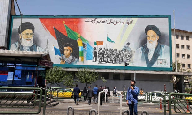 Iranians walk past a billboard bearing the portraits of supreme leader Ali Khamenei, left, and his late predecessor Ruhollah Khomeini