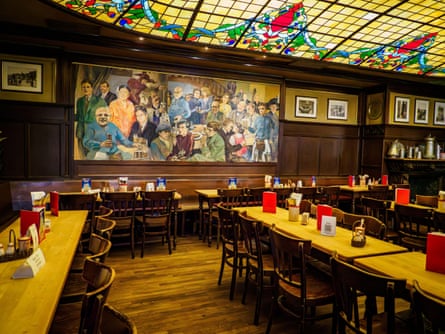 A room with stained glass ceiling, large painting of a bar scene and wooden panelling, tables and chairs