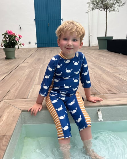 Oakley sits on the edge of a swimming pool, his feet in the water
