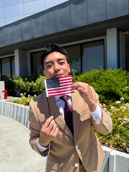 A smiling man in a beige suit holding a small American flag.