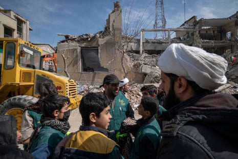 People gather in front of a building that is damaged