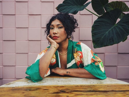 Portrait of Simone Ledward Boseman wearing a colourful dress, leaning on a table, with leaves of a green plant in the corner of the image
