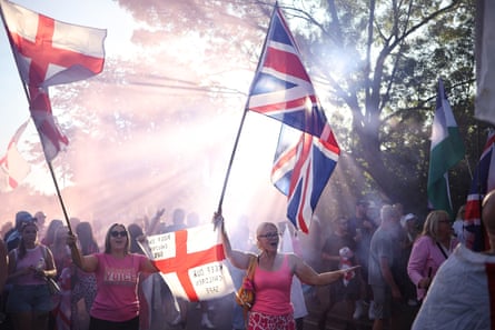 Women holding large union jack and England flags march down a tree-lined street