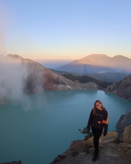 Young women stands in front of lake surrounded by mountains