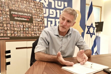 Yair Golan speaks sitting at a table in front of a poster calling for the release of hostages and an Israeli flag. He is in his early 60s with short grey hair and beard, and wears an open-necked shirt with the sleeves rolled up.