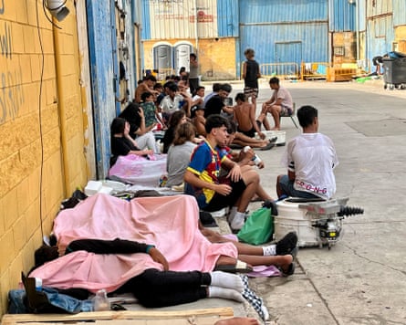 People sit or lie next to a wall on a street