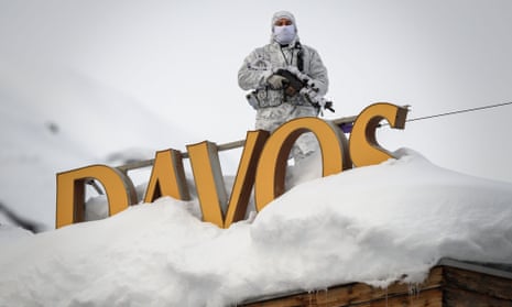 A police officer with an assault rifle and wearing snow camouflage, stands behind a large freestanding sign saying 'Davos'
