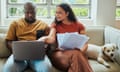 A young interracial couple working on their budget and finances on a sofa from home with their dog using a laptop computer, stock photo
