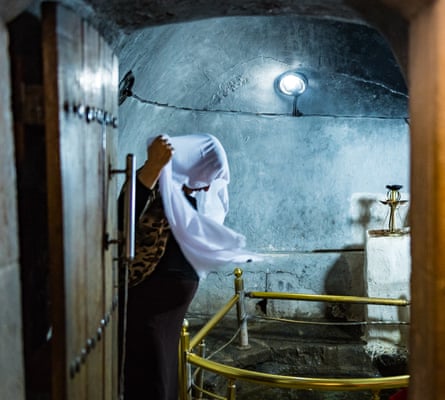 A woman covers her head with a white headscarf which has been bathed in the sacred spring.
