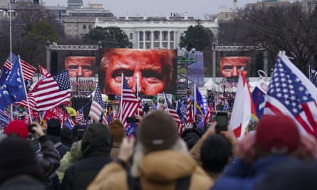 Trump supporters waving American flags attend the rally on 6 January in Washington DC. Three jumbo screens project a severe closeup of Donald Trump