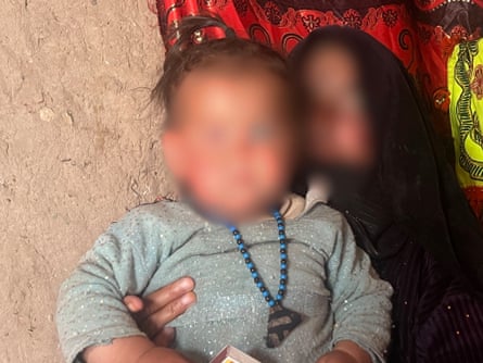The blurred faces of a toddler and her grandmother, who are sitting in a small hut