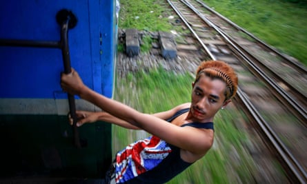 A young man hangs from a moving train in Yangon’s suburbs.