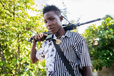A young Haitian man with a rifle over his shoulder looking at the camera