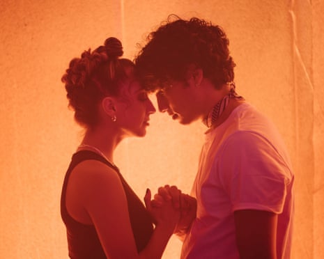 Two people stand forehead to forehead holding hands in warm orange light