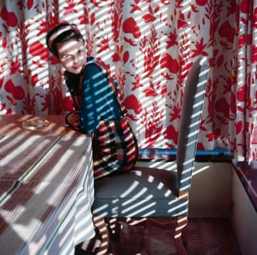 A woman sits at a table with a striped cloth and red and white patterned curtains behind her