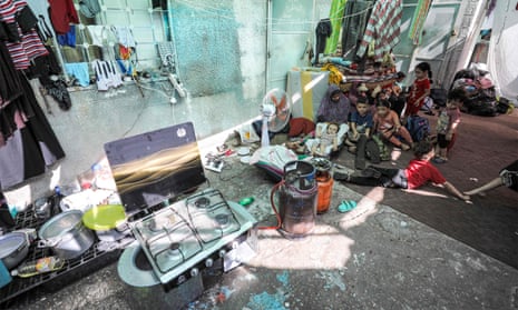 Women and children sit on a rug in the grounds of the hospital, with cooking equipment beside them