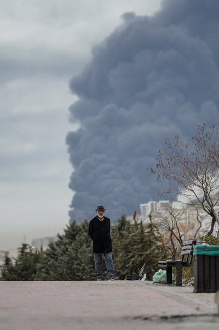 A man walks in a park with smoke rising after an airstrike.