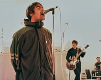 Liam Gallagher sings into a microphone as Noel Gallagher plays guitar behind him