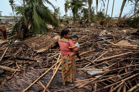 A Rohingya woman holds her baby next to her destroyed house at Basara refugee camp in Sittwe.