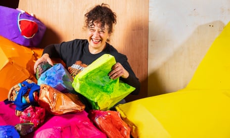 A woman smiling while holding brightly coloured artworks in the shape of rocks.