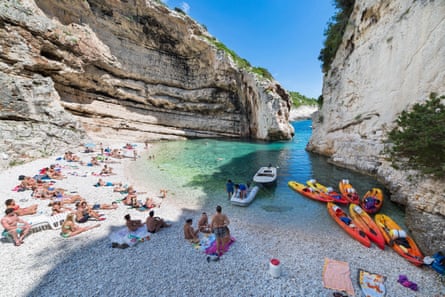 A small cove with sandy beach, sunbathers and moored kayaks and a a pool of shallow turquoise sea tucked between white cliffs