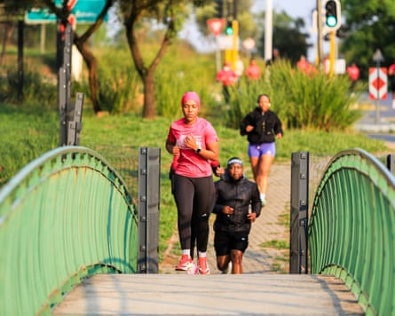 A woman in pink running gear crosses a bridge with a male runner in black following her