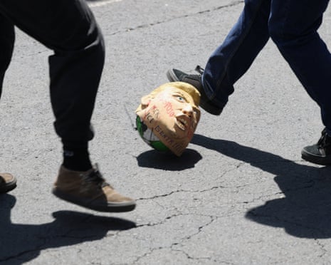 Protesters kick a ball covered with a mask representing Donald Trump while playing football on a major urban highway to protest against the reopening of Azteca Stadium.