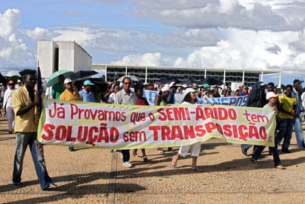 A few dozen demonstrators holding banners in front of a wide modernist building