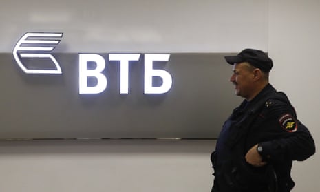 A police officer stands guard near a sign with the logo of the Russian lender VTB in Moscow
