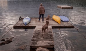 A rear view of William Wegman and his two Weimaraners, Flo and Topper, standing on a jetty in the lake