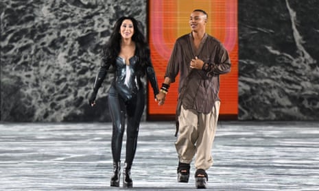 Cher walking on fashion runway in silver bodysuit holding hands with designer