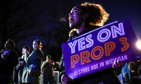 A woman holds a sign in support of Proposition 3 that reads 'Restore Roe in Michigan'.