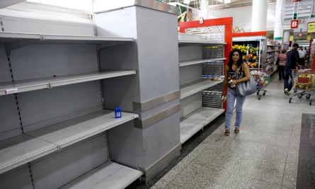 A woman walks past empty shelves where toilet paper should be displayed in a supermarket in Caracas.