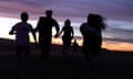 Five silhouetted young figures running towards a sunset