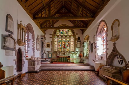 The interior of a medieval church with a stained glass window and wooden beams.