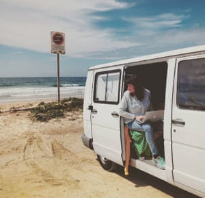Woman working  on laptop out of a van on a beach