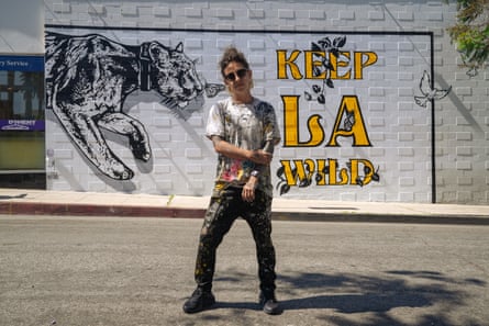 Woman stands in front of a painting on a building wall with a picture of p-22 and the phrase “keep LA wild”
