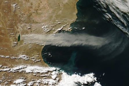 An aerial image showing a thick and feathery plume streaking horizontally across the middle of the image, originating from a dark blue blob, which is the lake, out over the ocean