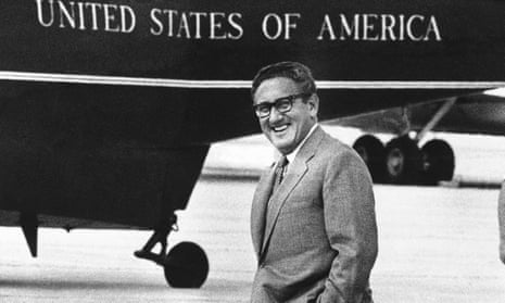 Henry Kissinger smiles and walks past helicopter with United States of America on the side