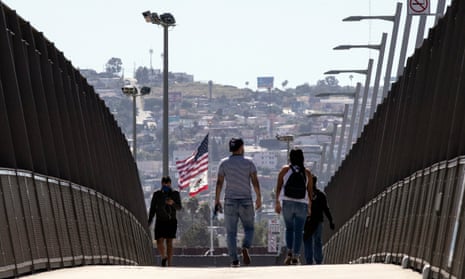 People wearing face masks cross the bridge over the freeway at the US-Mexico border in San Diego, California. 