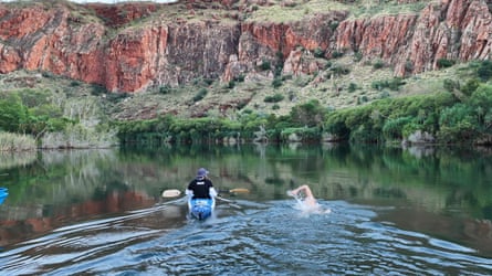 Andy Donaldson swims next to his support kayak on the Ord River with a view of the red-rock landscape either side