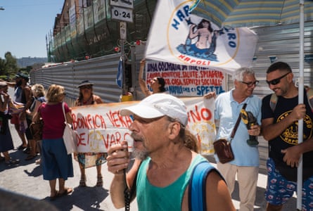 A man speaks into a megaphone while people stand behind him holding flags and banners