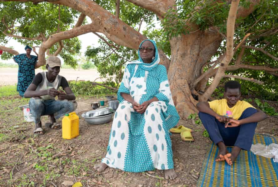An old woman in a long robe sits under a tree with two boys 