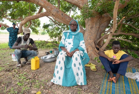 Une vieille femme en robe longue est assise sous un arbre avec deux garçons 